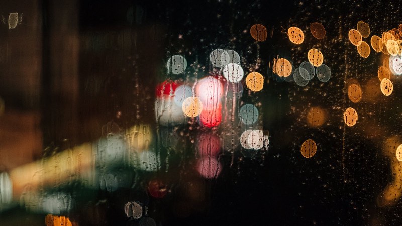 雨粒の付いた窓越しの夜の街の明かり